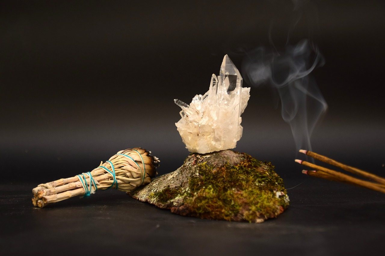 Druse de quartz posée sur une pierre, bâton de sauge et encens qui fume